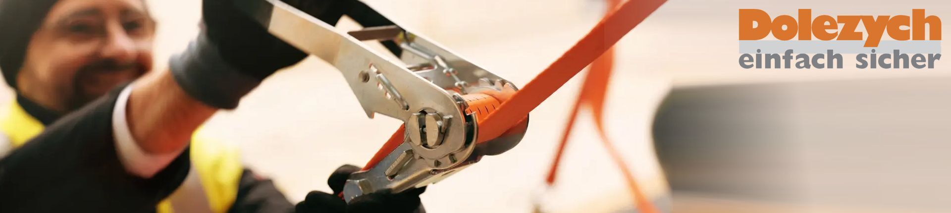 Ein Mann spannt einen orangefarbenen Zurrgurt von Dolezych an Ein Mann spannt einen orangefarbenen Zurrgurt von Dolezych an