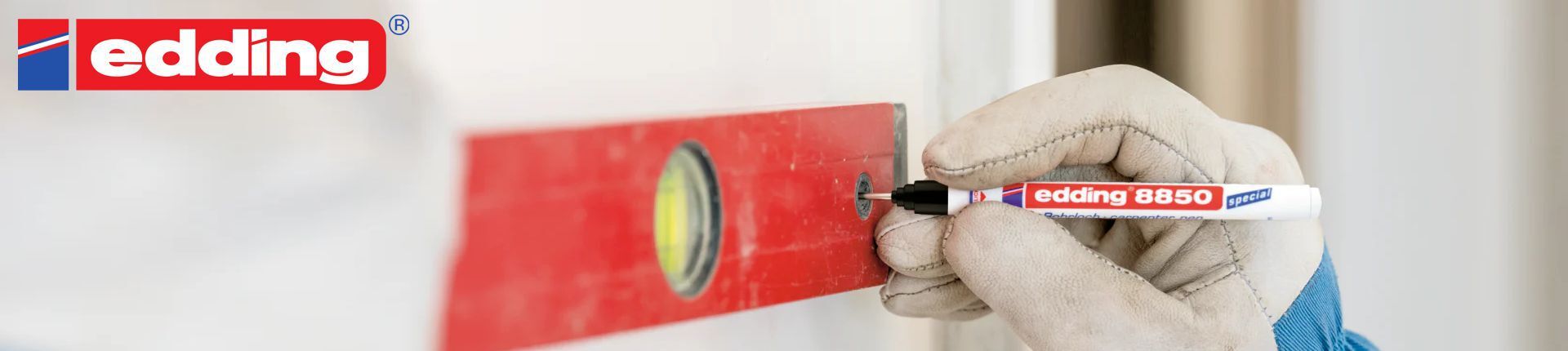 Special Edding im Einsatz beim Anzeichnen einer Markierung an einer beige-grauen Wand mit Hilfe einer roten Wasserwaage Special Edding im Einsatz beim Anzeichnen einer Markierung an einer beige-grauen Wand mit Hilfe einer roten Wasserwaage