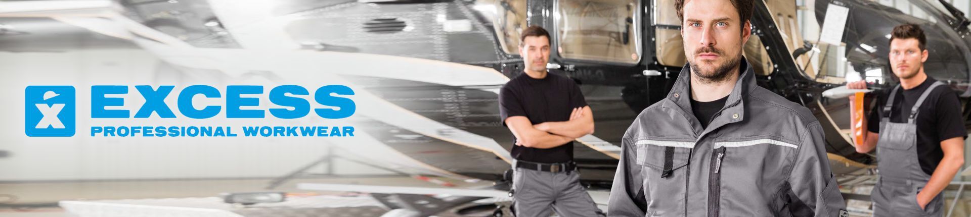 Drei Männer in Excess Grey Arbeitskleidung vor einem in einem Hangar stehenden Hubschrauber Drei Männer in Excess Grey Arbeitskleidung vor einem in einem Hangar stehenden Hubschrauber