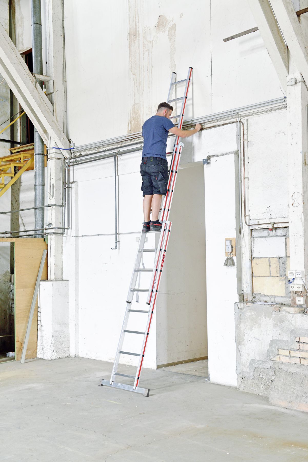 Handwerker auf einer dreiteiligen Mehrzweckleiter von Hymer stehend bei Arbeiten an einer wandmontierten Leitung