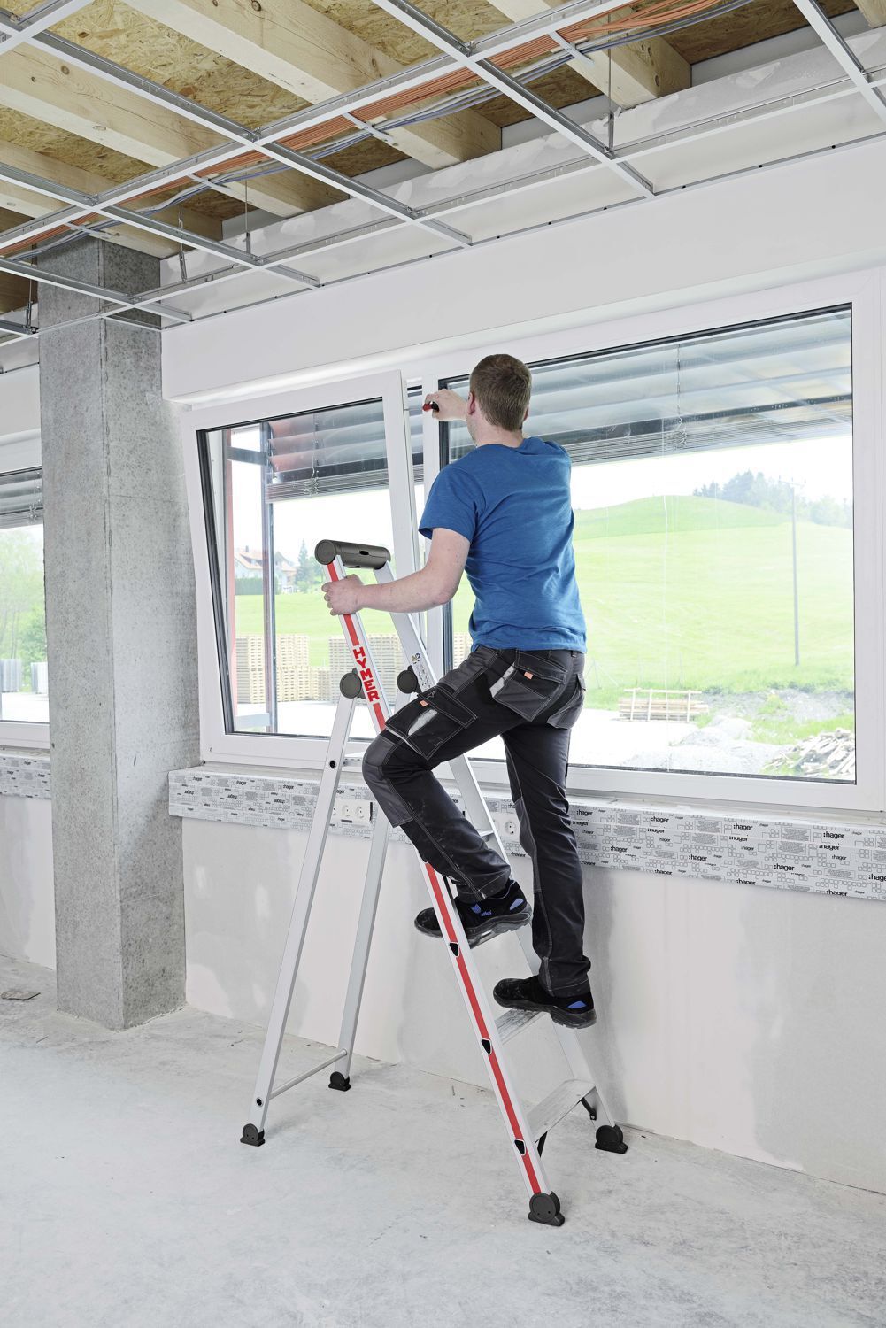  Fensterbauer in einem Rohbau bei der Montage auf einer Hymer Stufenstehleiter Plattform einseitig 5 Stufen Modell 402605 stehend