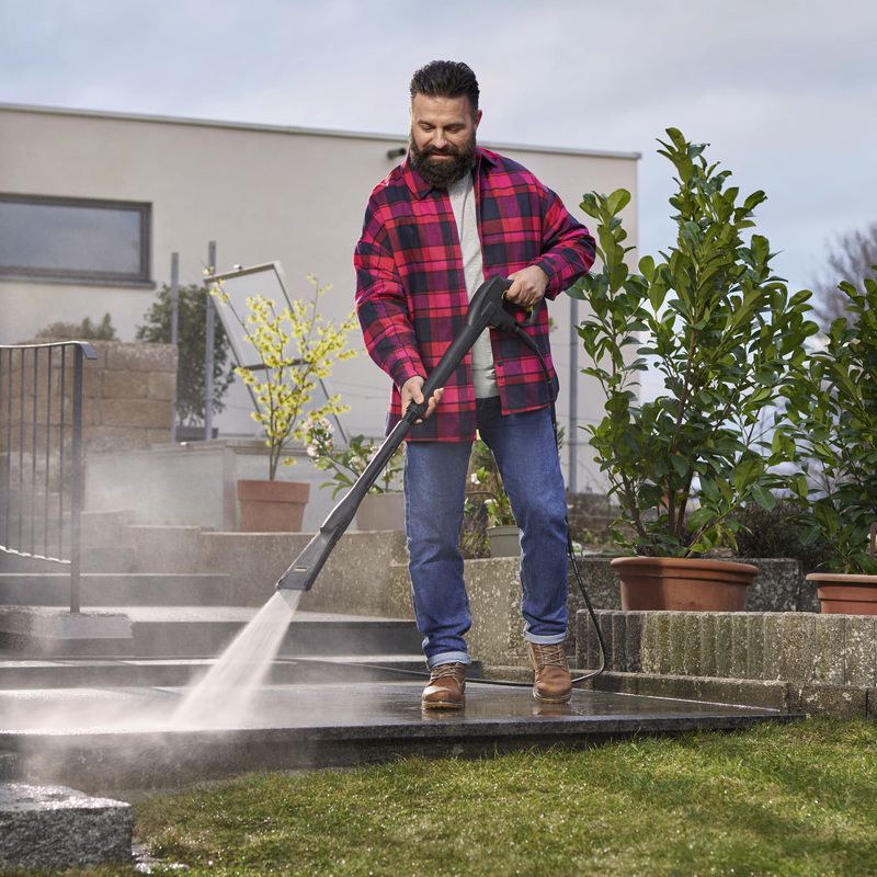 Kärcher Eco Booster im Einsatz bei der Terrassenreinigung Mann mit dunklem Bart und dunklen kurzen Haaren reinigt eine Steinterrasse mit einem Kärcher eco Booster