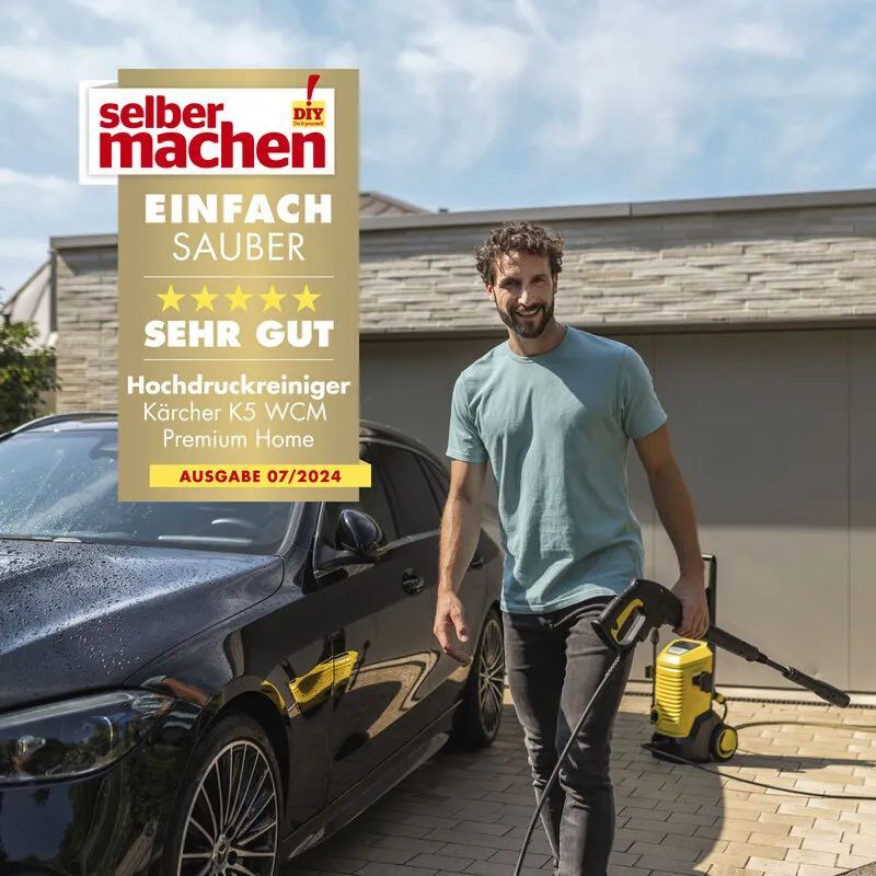 Kärcher Hochdruckreiniger K 5 WCM Premium Home Selber machen Testurteil Ein Mann läuft mit einem Kärcher K5 WCM Premium Home Hochdruckreiniger über den Hof auf dem ein schwarzes Auto geparkt ist
