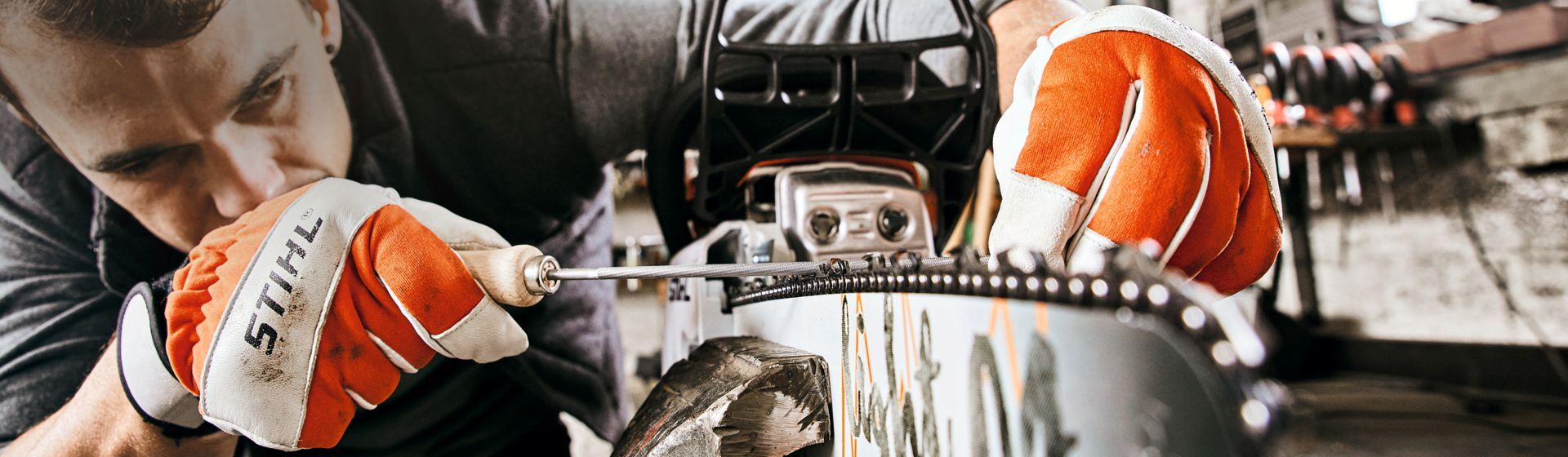 Mann mit Stihl Arbeitshandschuhen beim Bearbeiten einer an eine Motorsäge montierte Sägekette Mann mit Stihl Arbeitshandschuhen beim Bearbeiten einer an eine Motorsäge montierte Sägekette