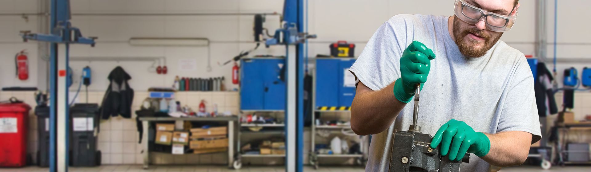 Junger Mann in einer Werkstatt mit grünen Einweghanschuhen von Ansell bei handwerklichen Arbeiten Junger Mann in einer Werkstatt mit grünen Einweghanschuhen von Ansell bei handwerklichen Arbeiten