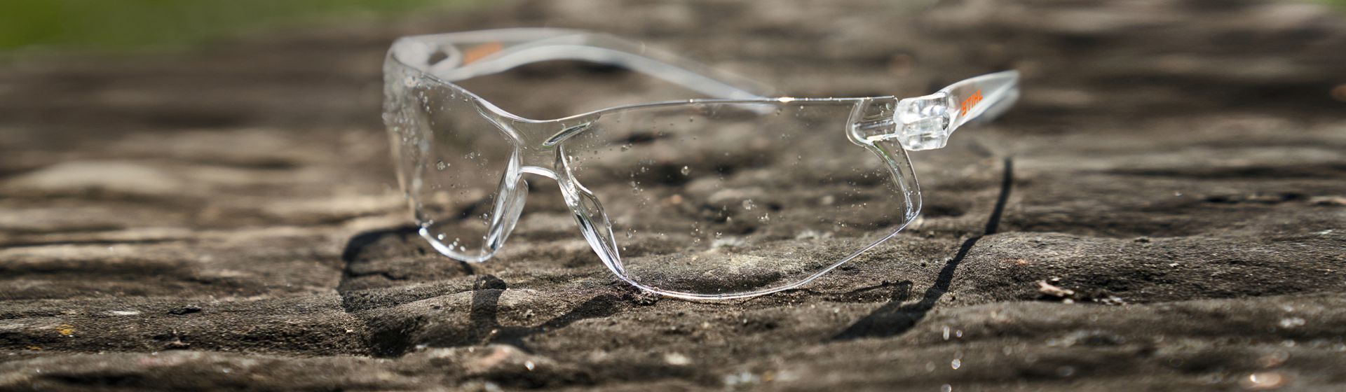 Transparente Schutzbrille von Stihl auf einem Stein liegend Transparente Schutzbrille von Stihl auf einem Stein liegend