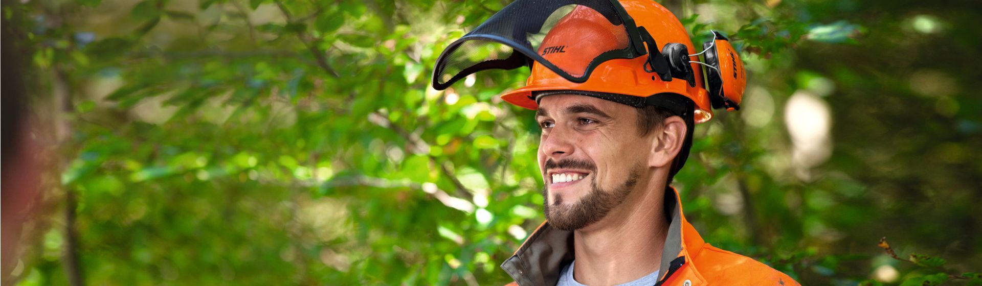 Junger Mann mit Stihl Schutzhelm mit Gehörschutkapseln und hochgeklapptem Visier Junger Mann mit Stihl Schutzhelm mit Gehörschutkapseln und hochgeklapptem Visier