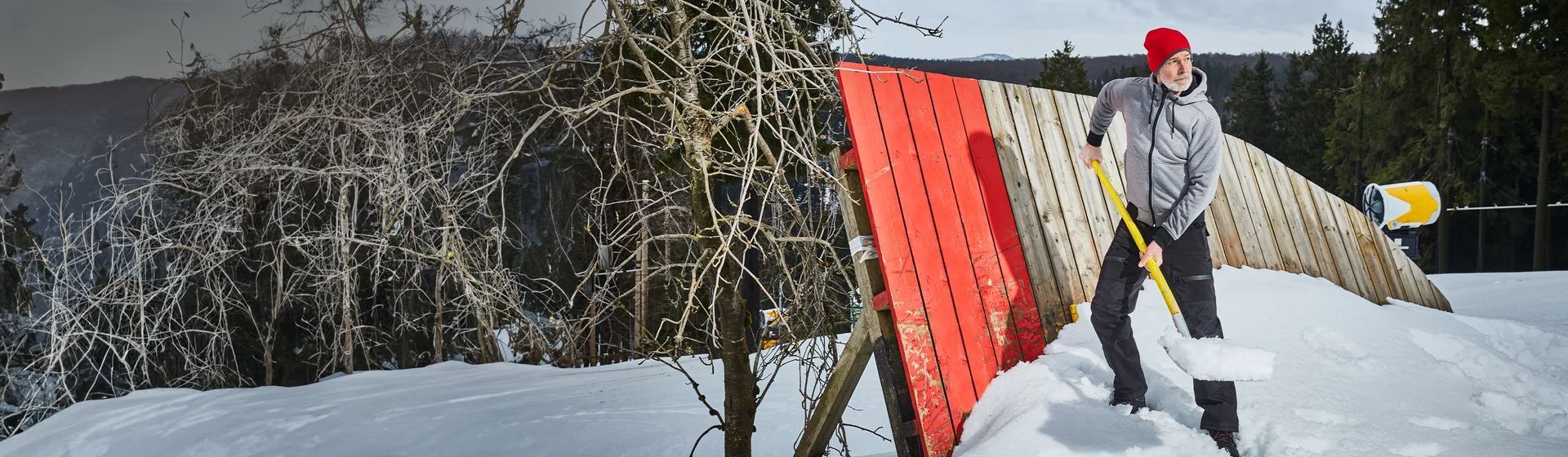 Mann in einer grauen Sweatjacke mit roter Woll-Mütze beim Schneeschippen Mann in einer grauen Sweatjacke mit roter Woll-Mütze beim Schneeschippen