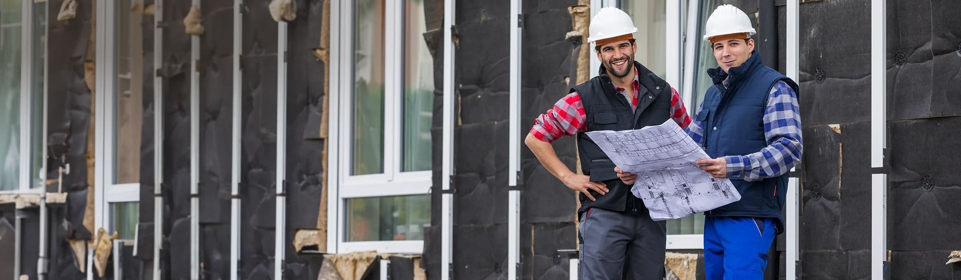 Zwei junge Handwerker in Arbeitkleidung mit karierten Hemd auf einer Baustelle Zwei junge Handwerker in Arbeitkleidung mit karierten Hemd auf einer Baustelle
