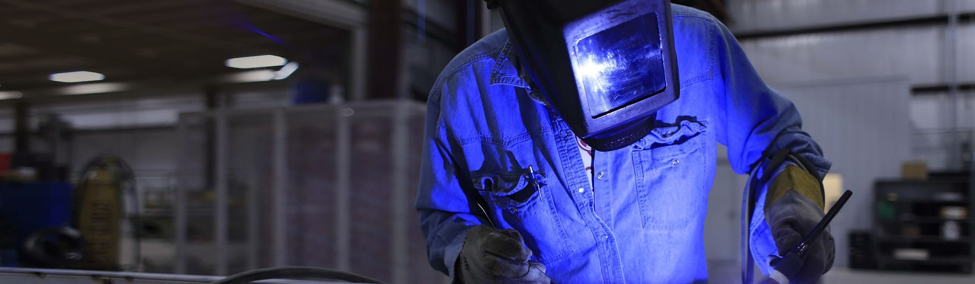 Schweißer in einem blauen Arbeitsoverall mit Schutzhandschuhe und Schutzvisier bei der Arbeit Schweißer in einem blauen Arbeitsoverall mit Schutzhandschuhe und Schutzvisier bei der Arbeit