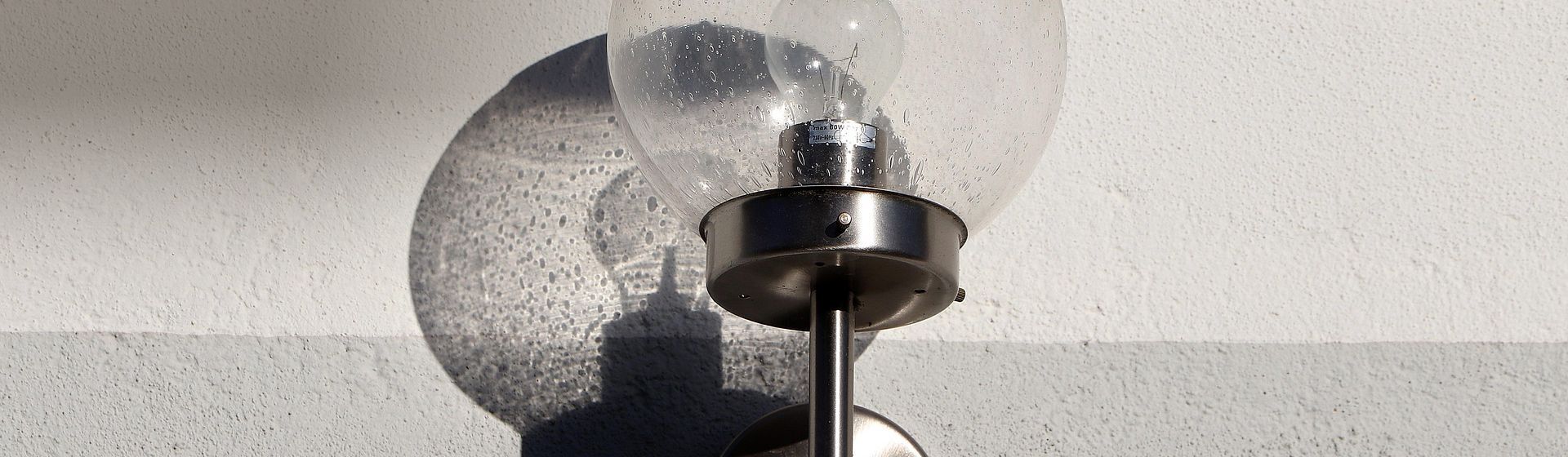 Wandleuchte mit rundem Lampenschirm aus Glas an einer weißen Hauswand hängend Wandleuchte mit rundem Lampenschirm aus Glas an einer weißen Hauswand hängend