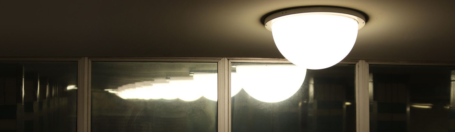 Weiße direkte Deckenleuchte in einem dunklen Raum gespiegelt in einem Fenster