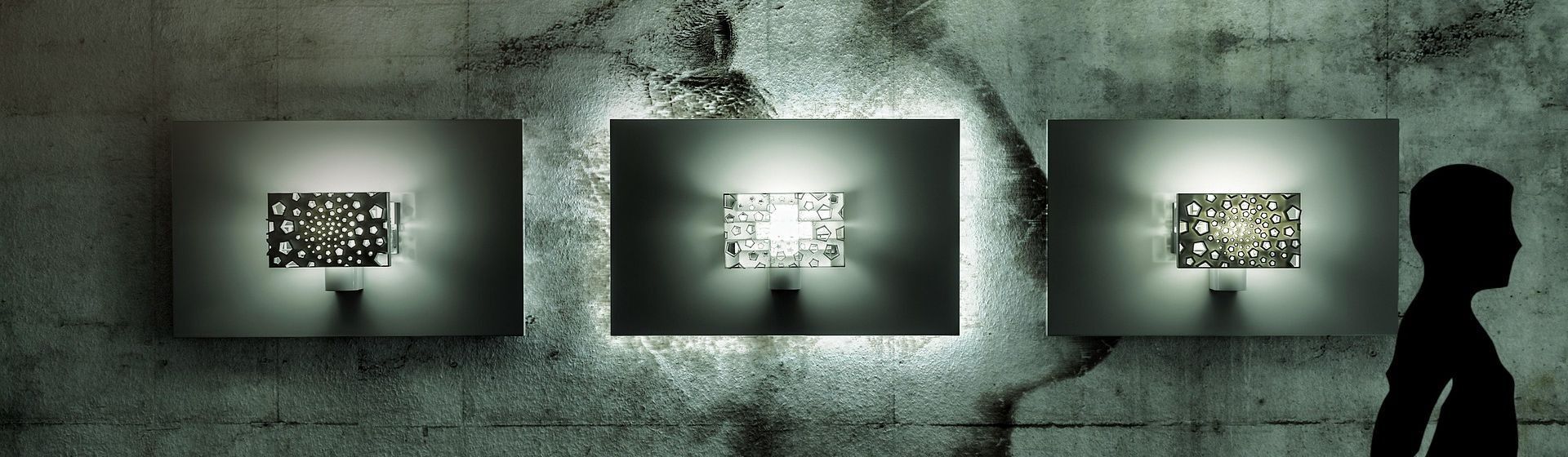 Drei silberfarbene Designer Wandleuchten an einer grauen Wand hängend Drei silberfarbene Designer Wandleuchten an einer grauen Wand hängend