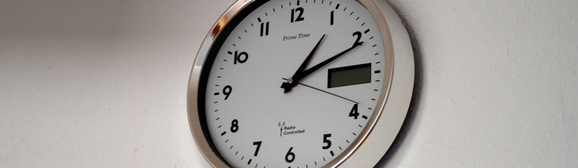 Wanduhr mit weißem Ziffernblatt und silbernem Rahmen an einer hellen Wand montiert Wanduhr mit weißem Ziffernblatt und silbernem Rahmen an einer hellen Wand montiert