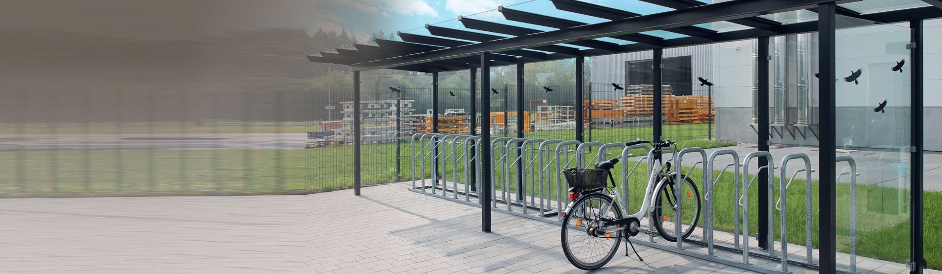 Überdachter WSM Fahrradständer mit einem weißen Damenrad vor einem Firmengebäude in einer industriellen Umgebung Überdachter WSM Fahrradständer mit einem weißen Damenrad vor einem Firmengebäude in einer industriellen Umgebung