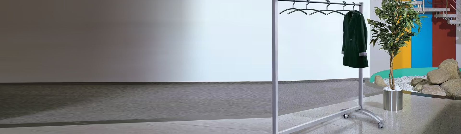 Silberfarbener Garderobenständer mit Kleiderbügeln bestückt, an dem eine grüne Damenjacke hängt, in einer Eingangshalle stehend Silberfarbener Garderobenständer mit Kleiderbügeln bestückt, an dem eine grüne Damenjacke hängt, in einer Eingangshalle stehend