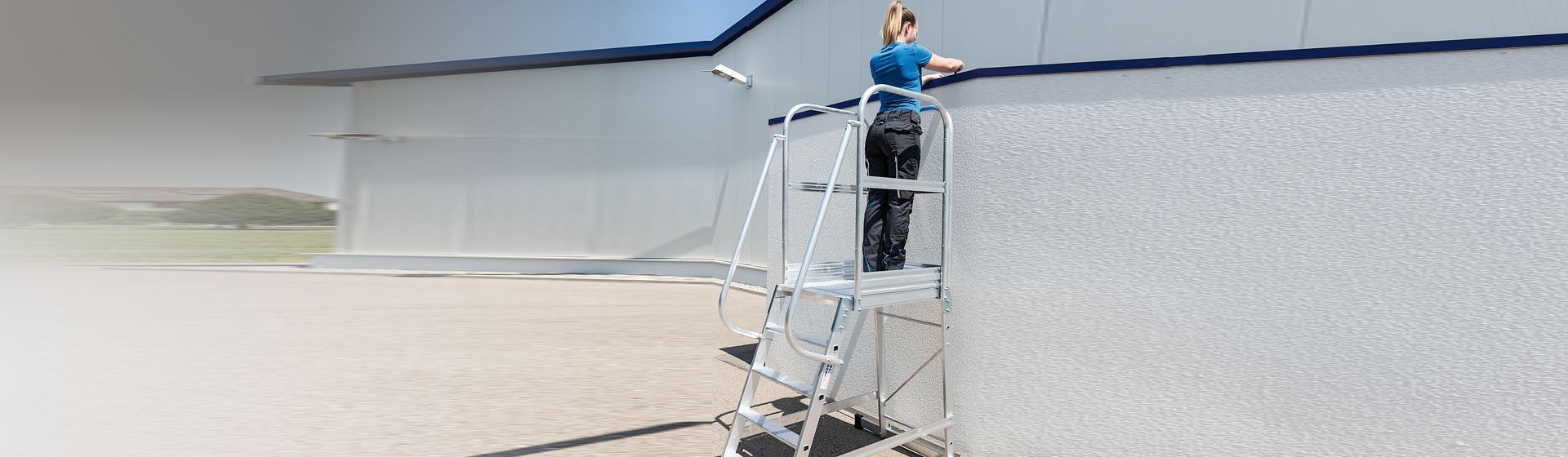 Handwerkerin auf einer Munk Plattformleiter bei Arbeiten an der Außenseite eines Gebäudes Handwerkerin auf einer Munk Plattformleiter bei Arbeiten an der Außenseite eines Gebäudes