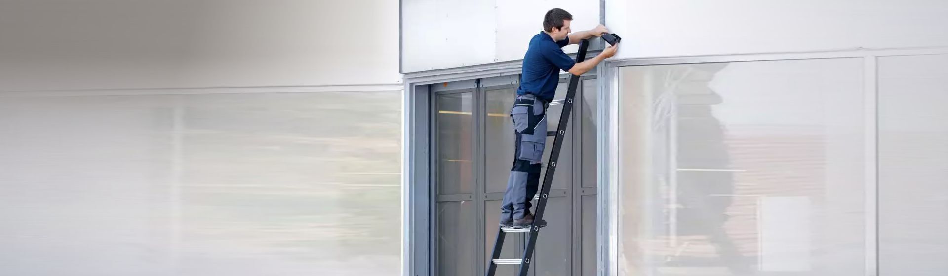 Handwerker bei Montagearbeiten auf einer an einer Fensterfront angelehnten Schwerlastleiter