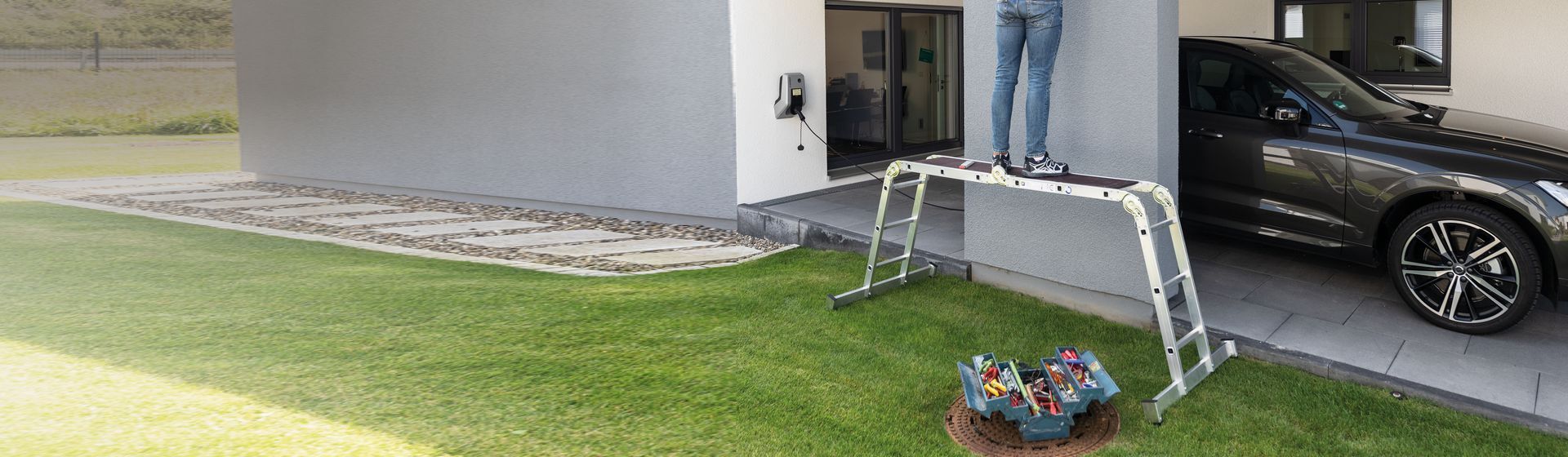 Mann auf einer Munk Vielzweckleiter auf einer Rasenfläche vor einer Garage