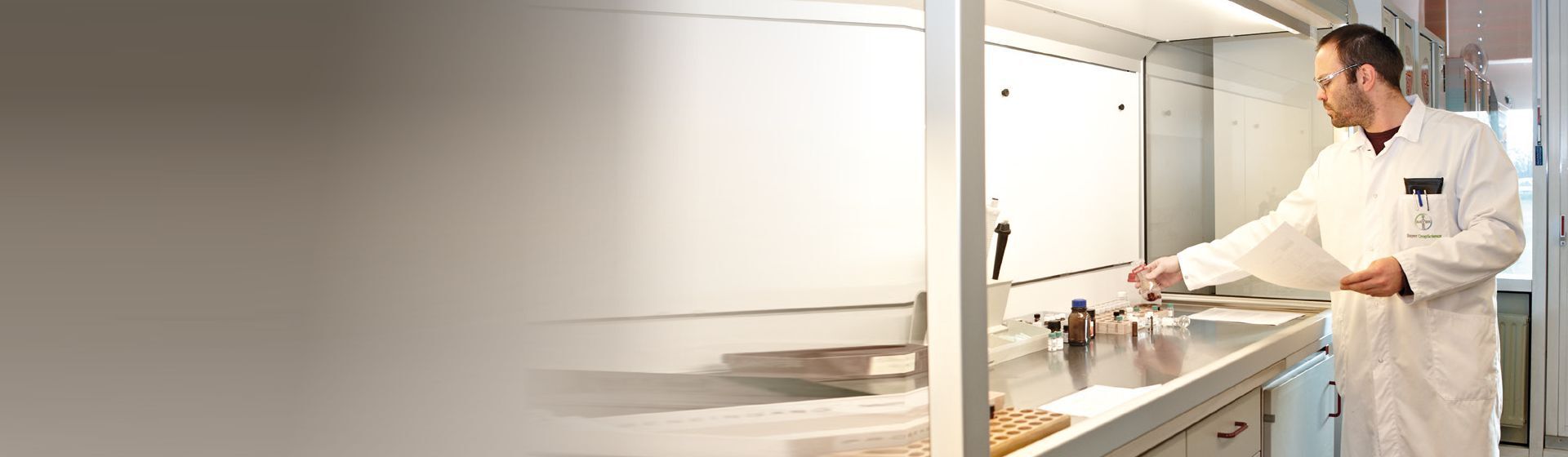 Mann mit Schutzbrille und weißem Arbeitskittel an einem Gefahrstoffarbeitsplatz Mann mit Schutzbrille und weißem Arbeitskittel an einem Gefahrstoffarbeitsplatz