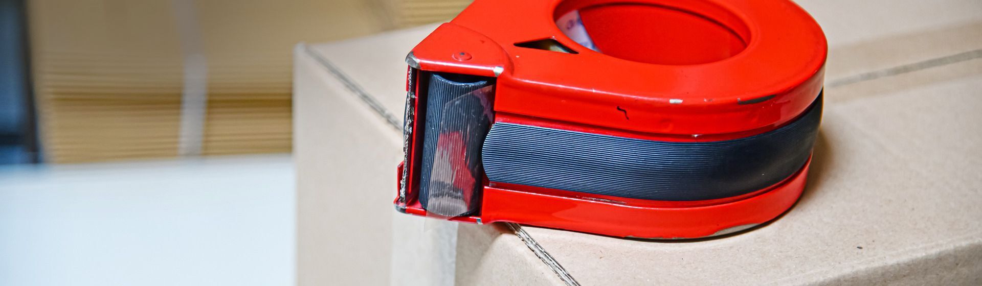 Roter Klebeband-Handabroller auf einem Paket liegend Roter Klebeband-Handabroller auf einem Paket liegend