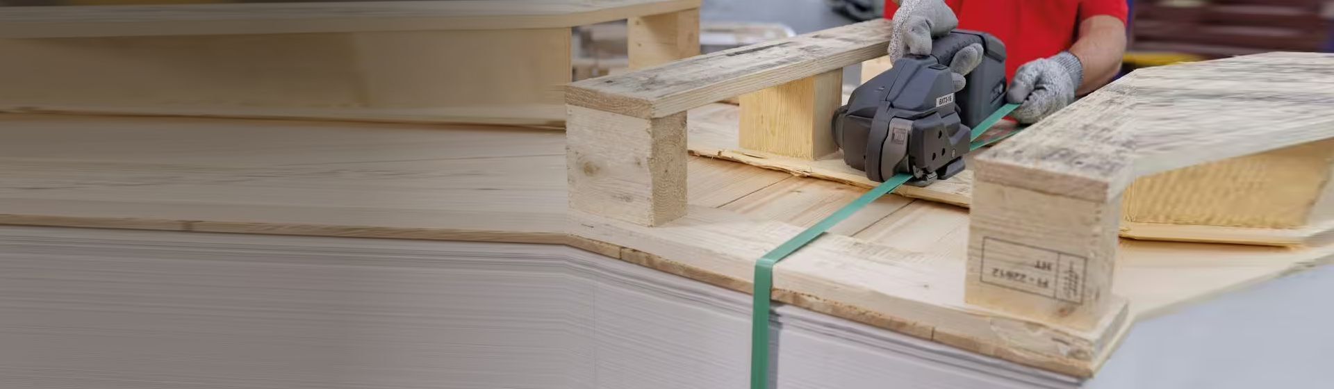 Grünes Kunststoffband wird mit einem Umreifungsgerät von Banholzer und Wenz an einer Palette angebracht Grünes Kunststoffband wird mit einem Umreifungsgerät von Banholzer und Wenz an einer Palette angebracht