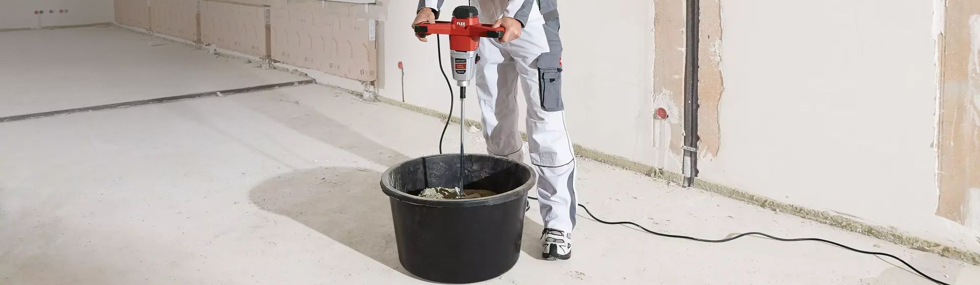 Handwerker mit einem Flex Rührwerk beim Anmischen von Beton in einem Eimer auf einer Baustelle Handwerker mit einem Flex Rührwerk beim Anmischen von Beton in einem Eimer auf einer Baustelle
