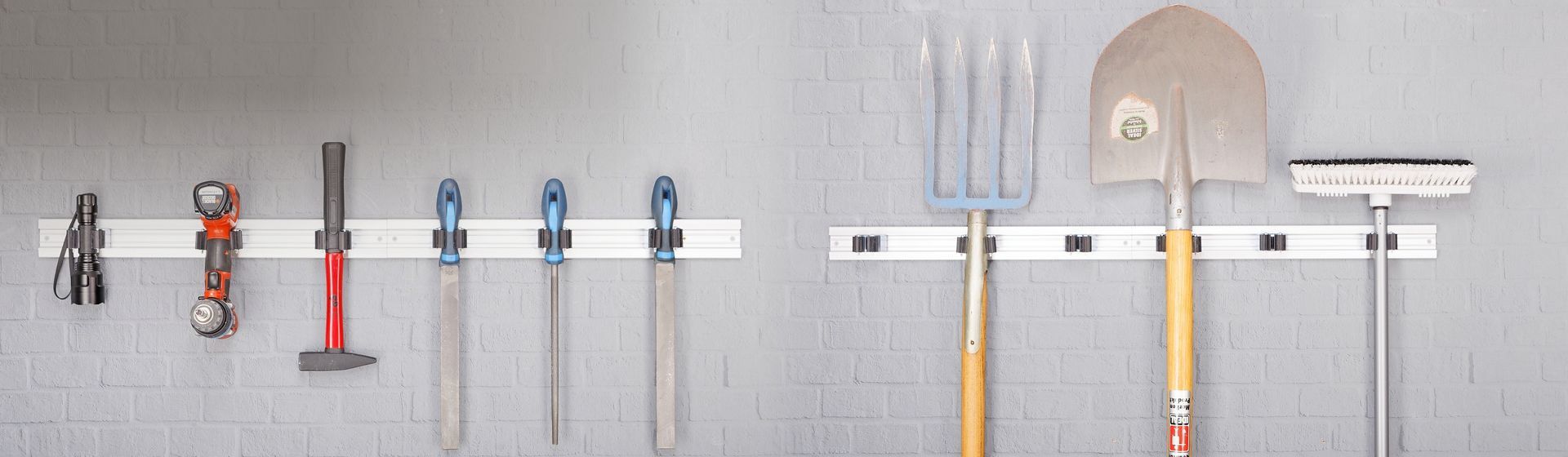 Diverse Garten- und Handwerkzeuge an einem an einer grauen Mauer montierten Gerätehalter hängend Diverse Garten- und Handwerkzeuge an einem an einer grauen Mauer montierten Gerätehalter hängend