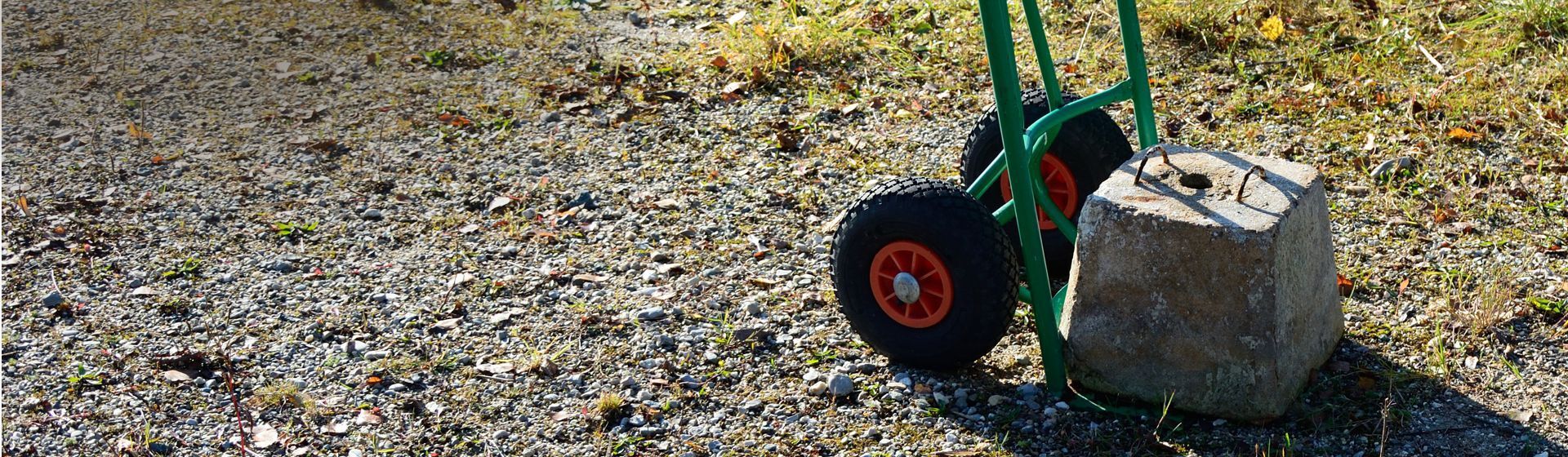 Grüne Sackkarre beladen mit einem Betonklotz auf einem Kieselsteinweg stehend Grüne Sackkarre beladen mit einem Betonklotz auf einem Kieselsteinweg stehend