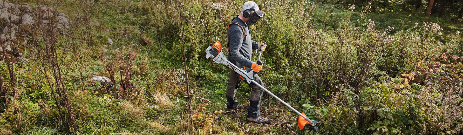 Mann mit Stihl Motorsense beim Mähen einer Wiese Mann mit Stihl Motorsense beim Mähen einer Wiese