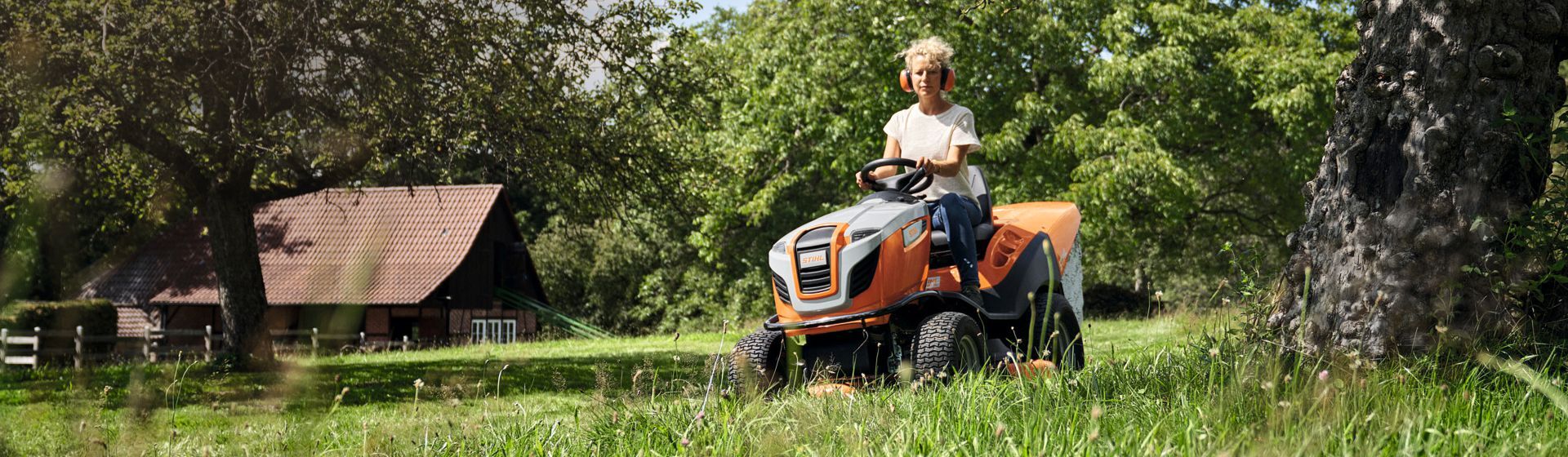 Frau auf einem Stihl Rasentraktor beim Mähen einer Wiese