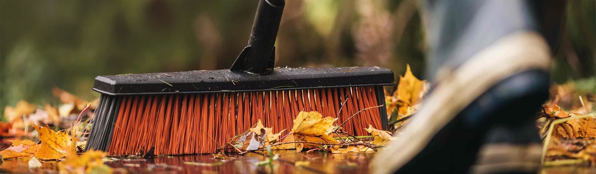 Schwarzer Kehrbesen von Fiskars mit roten Borsten beim Wegfegen von Herbstlaub