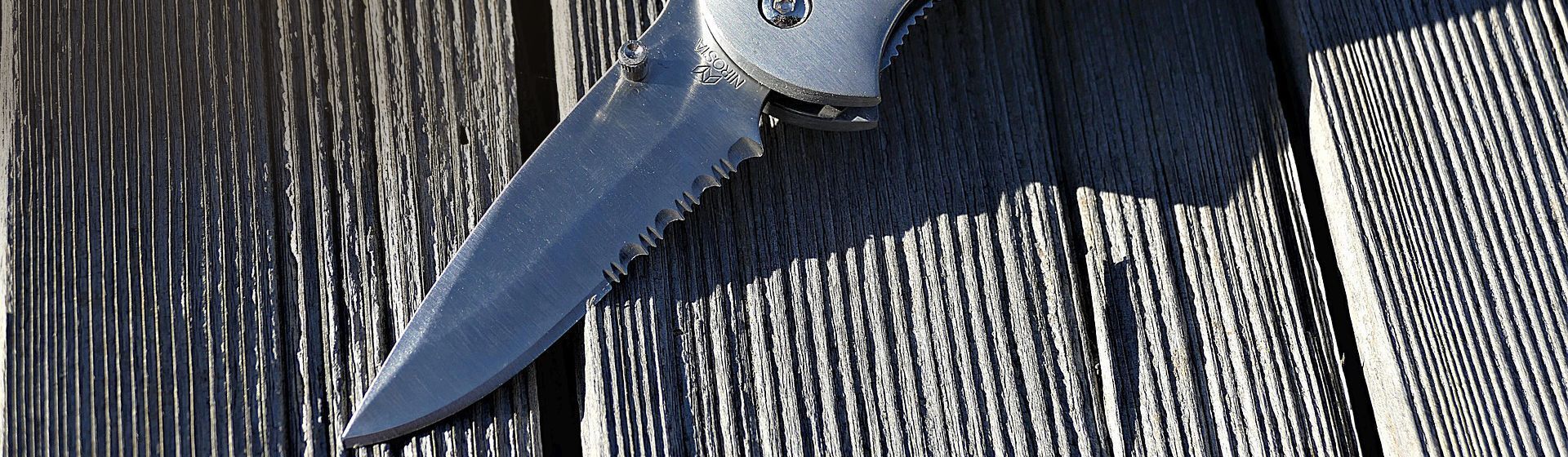 Silberfarbenes Klappmesser auf einem Holzboden in der Sonne liegend