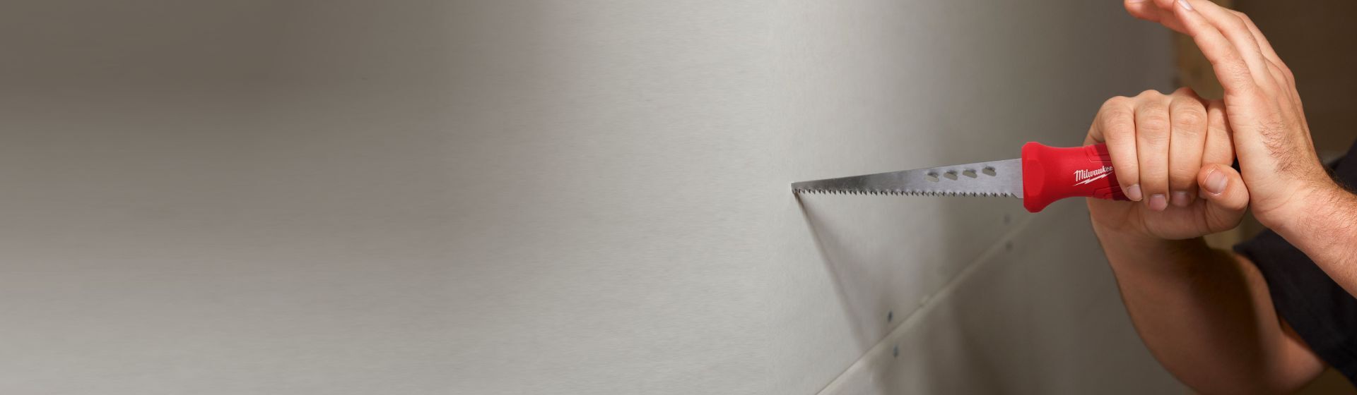 Mann bearbeitet eine weiße Gipskartonwand mit einer Stichsäge von Milwaukee Mann bearbeitet eine weiße Gipskartonwand mit einer Stichsäge von Milwaukee