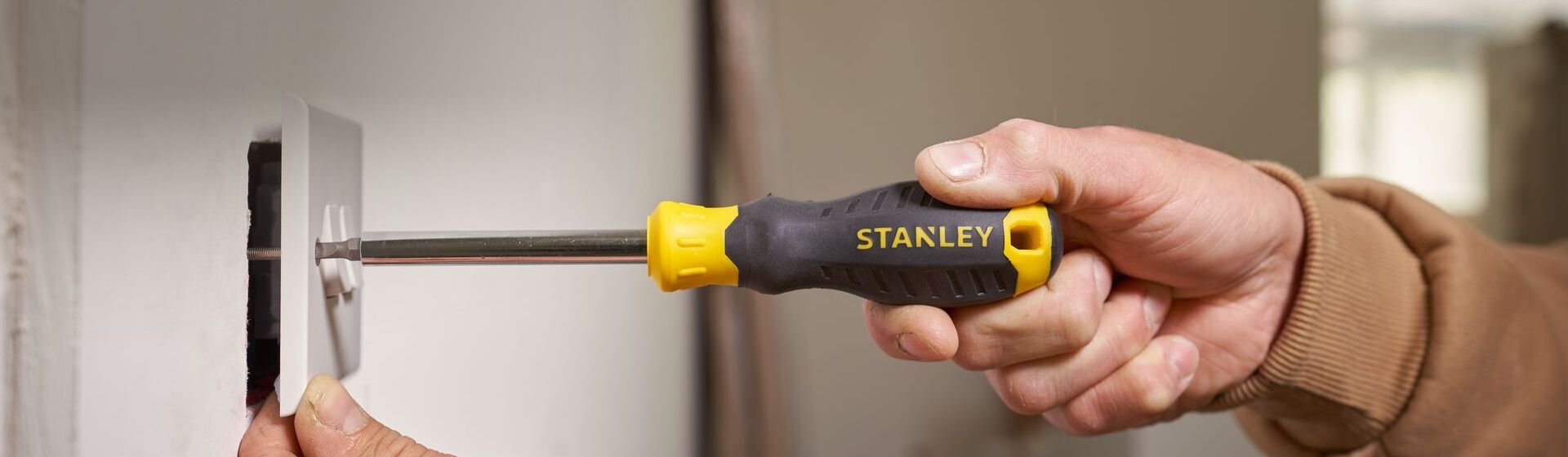 Handwerker befestigt eine weiße Schalterabdeckung mit einem Schlitz-Schraubendreher von Stanley Handwerker befestigt eine weiße Schalterabdeckung mit einem Schlitz-Schraubendreher von Stanley