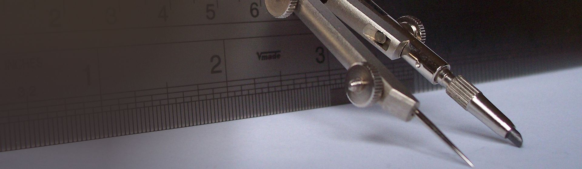 Silberfarbener Zirkel an einem Metall-Lineal angelehnt