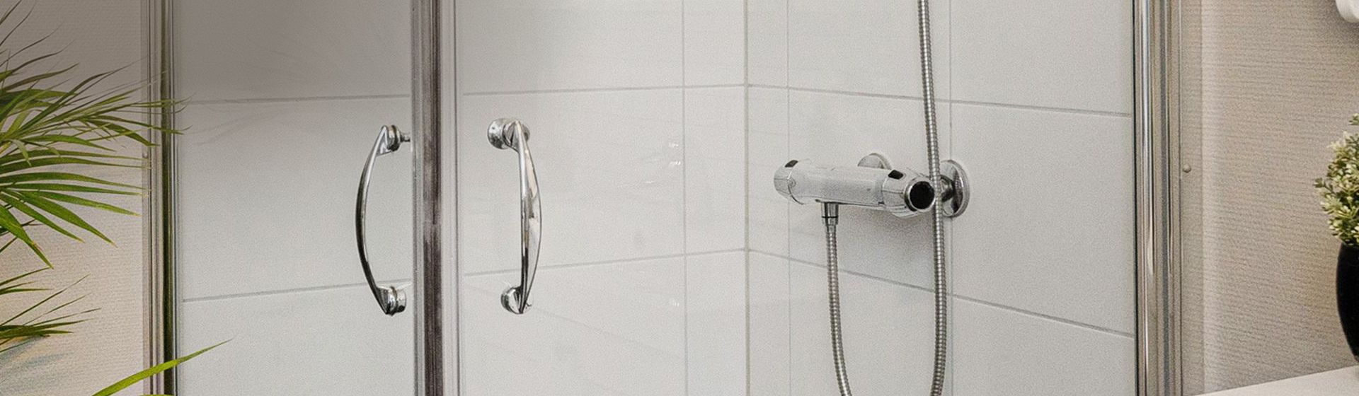 Blick auf eine silberfarbene Thermostatbatterie in einer weiß gefliesten Dusche Blick auf eine silberfarbene Thermostatbatterie in einer weiß gefliesten Dusche