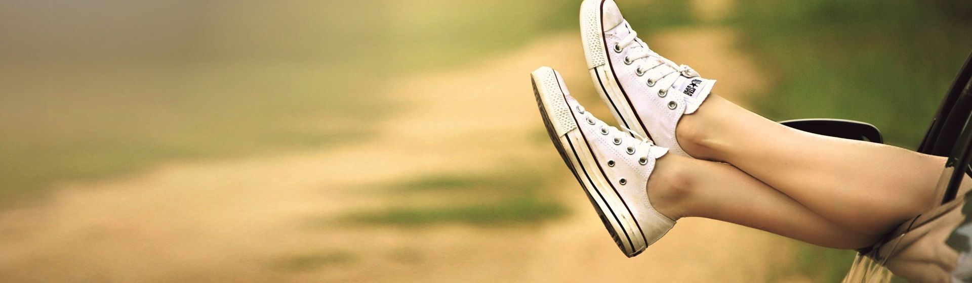 Weibliche Beine mit weißen Sneakern an den Füßen, die aus einem offenen Autofenster hinausgestreckt werden Weibliche Beine mit weißen Sneakern an den Füßen, die aus einem offenen Autofenster hinausgestreckt werden