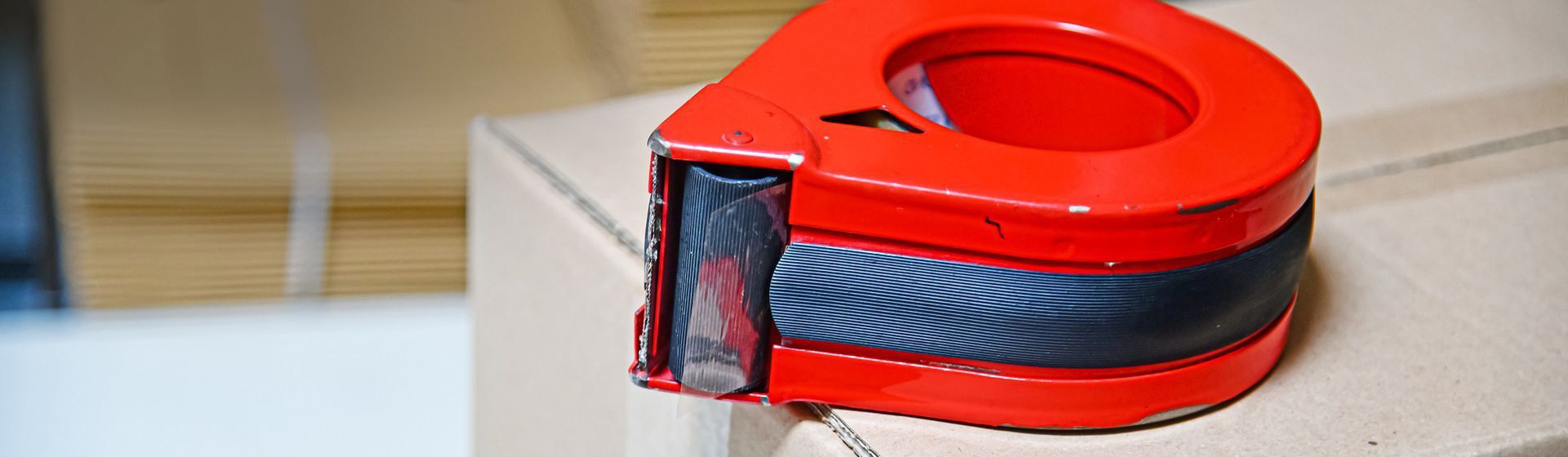 Roter Klebebandabroller bestückt mit transparentem Klebeband auf einem Karton liegend