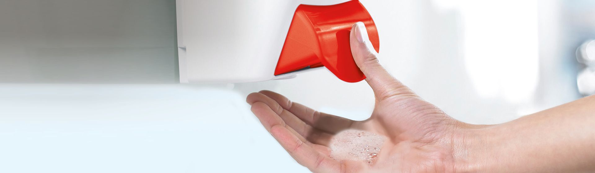 Weibliche Hand entnimmt Seife aus einem weißen an einer Wand montierten Seifenspender