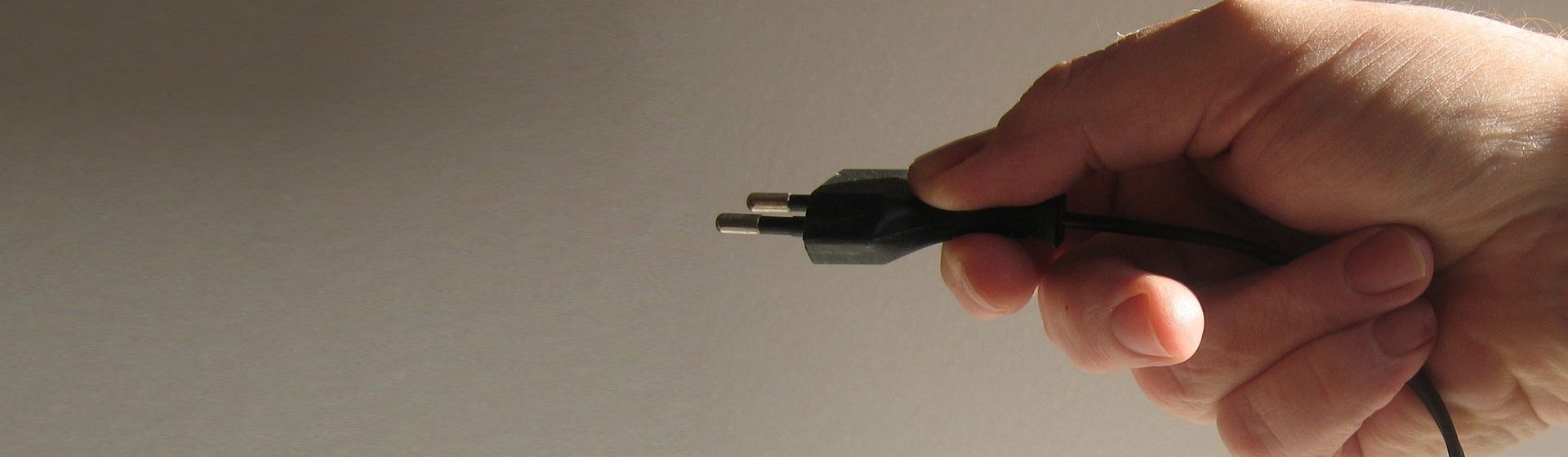 Schwarzes Netzkabel mit Schuko-Stecker in einer menschlichen Hand gehalten